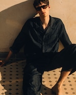Placeholder for: Man in textured co-ord with sunglasses on sitting on the floor against a wall