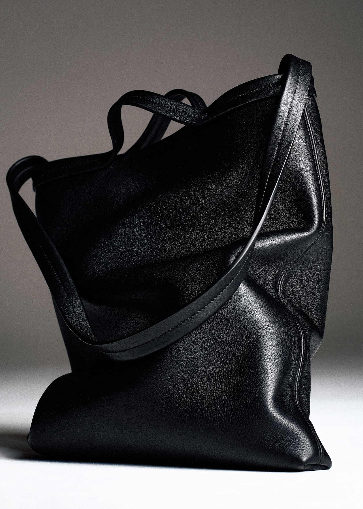 A sleek black leather tote bag with two handles, positioned against a neutral background.