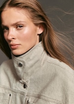 Placeholder for: Woman with light brown hair wearing a high-collared beige jacket, looking intently at the camera against a neutral background.