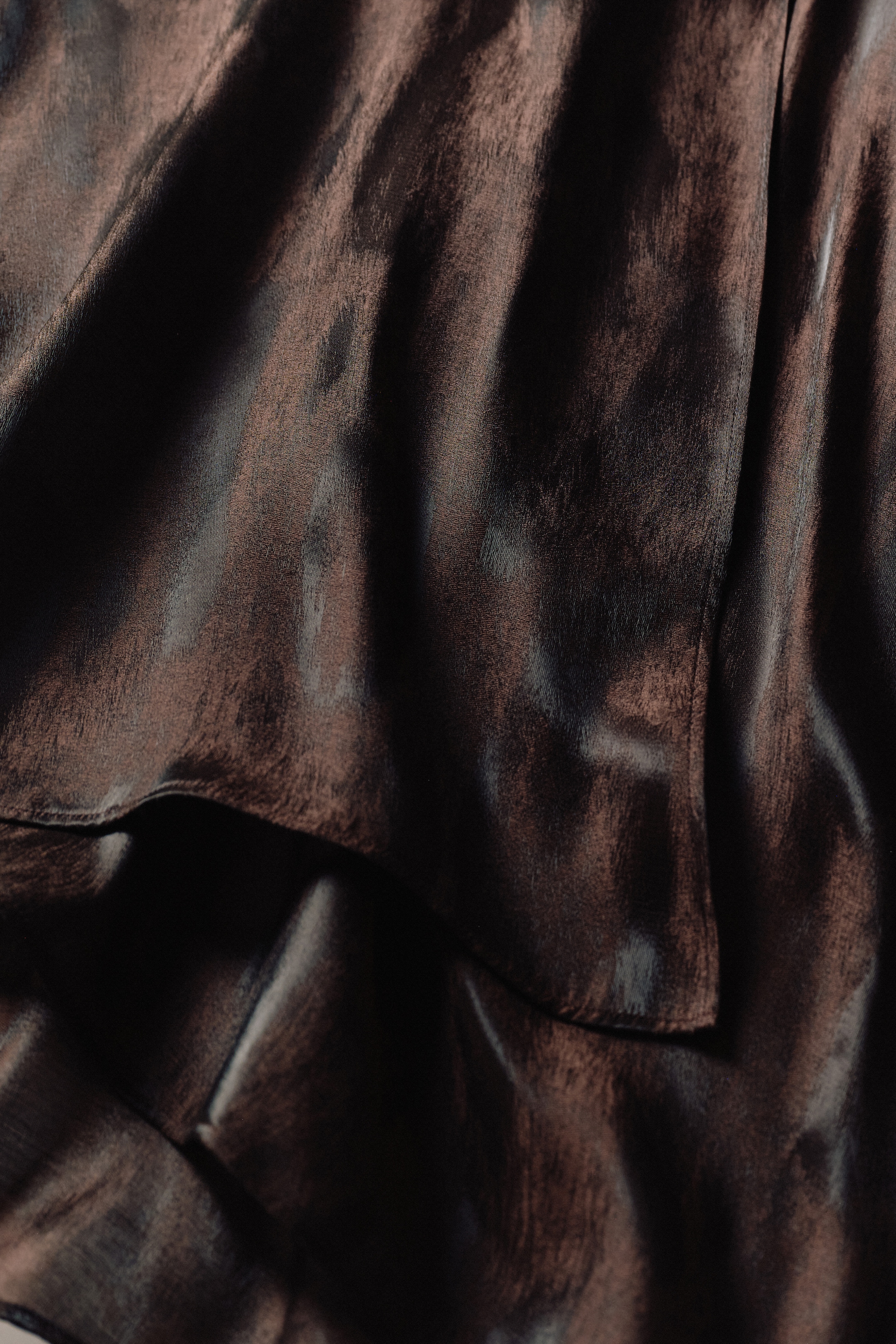 Close-up of dark, glossy fabric with soft, flowing folds and a smooth texture, creating a luxurious appearance.