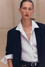 Placeholder for: Person wearing a black blazer over a white pinstriped shirt, with sleeves rolled up, looking upward with a neutral expression.