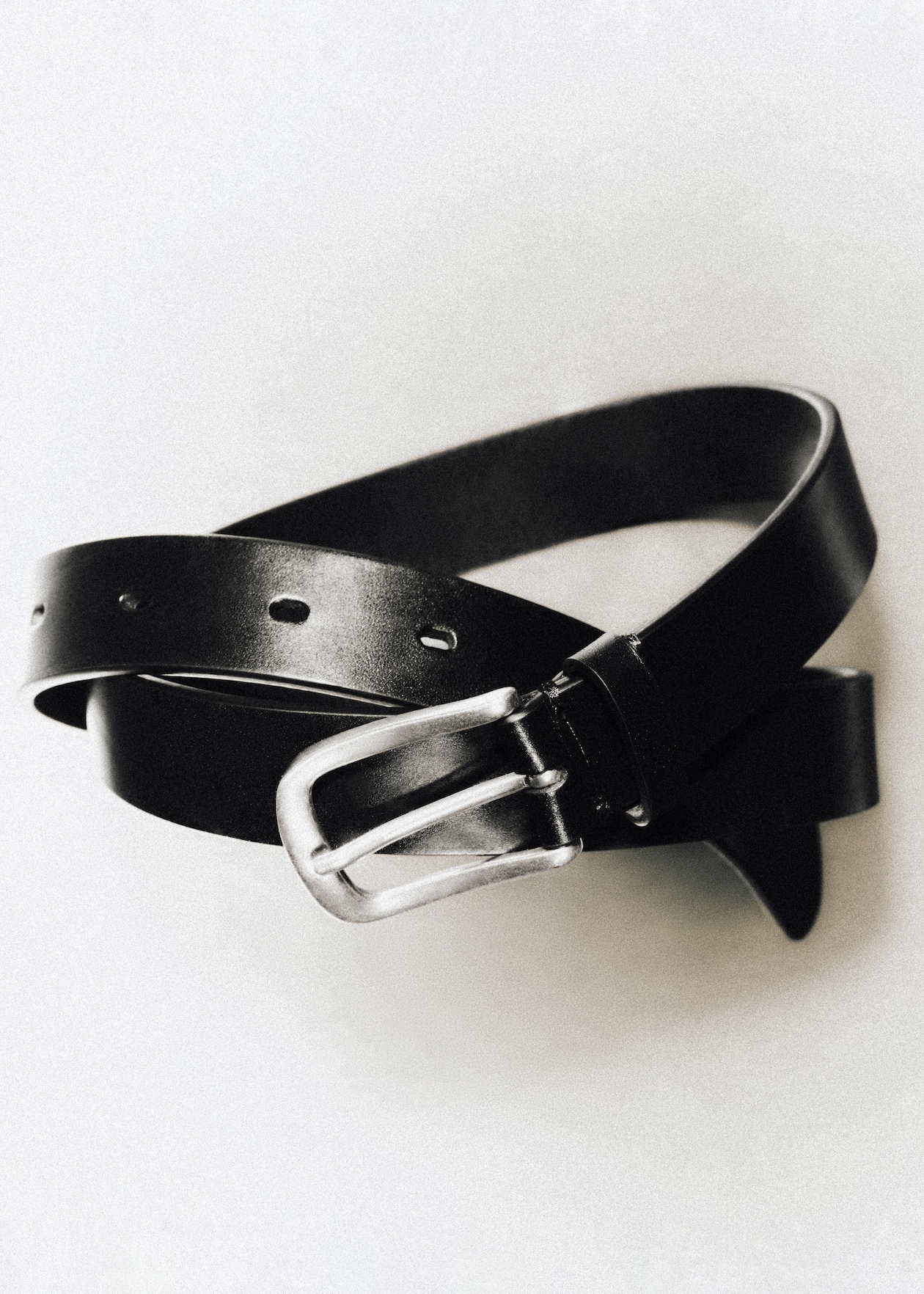 A black leather belt with a silver buckle coiled on a light background.