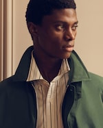 Placeholder for: A person in a striped shirt and green jacket gazing to the side with a thoughtful expression.