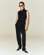 Placeholder for: Person wearing a stylish black sleeveless top and pants, sunglasses, and pointed shoes, posing against a plain background.