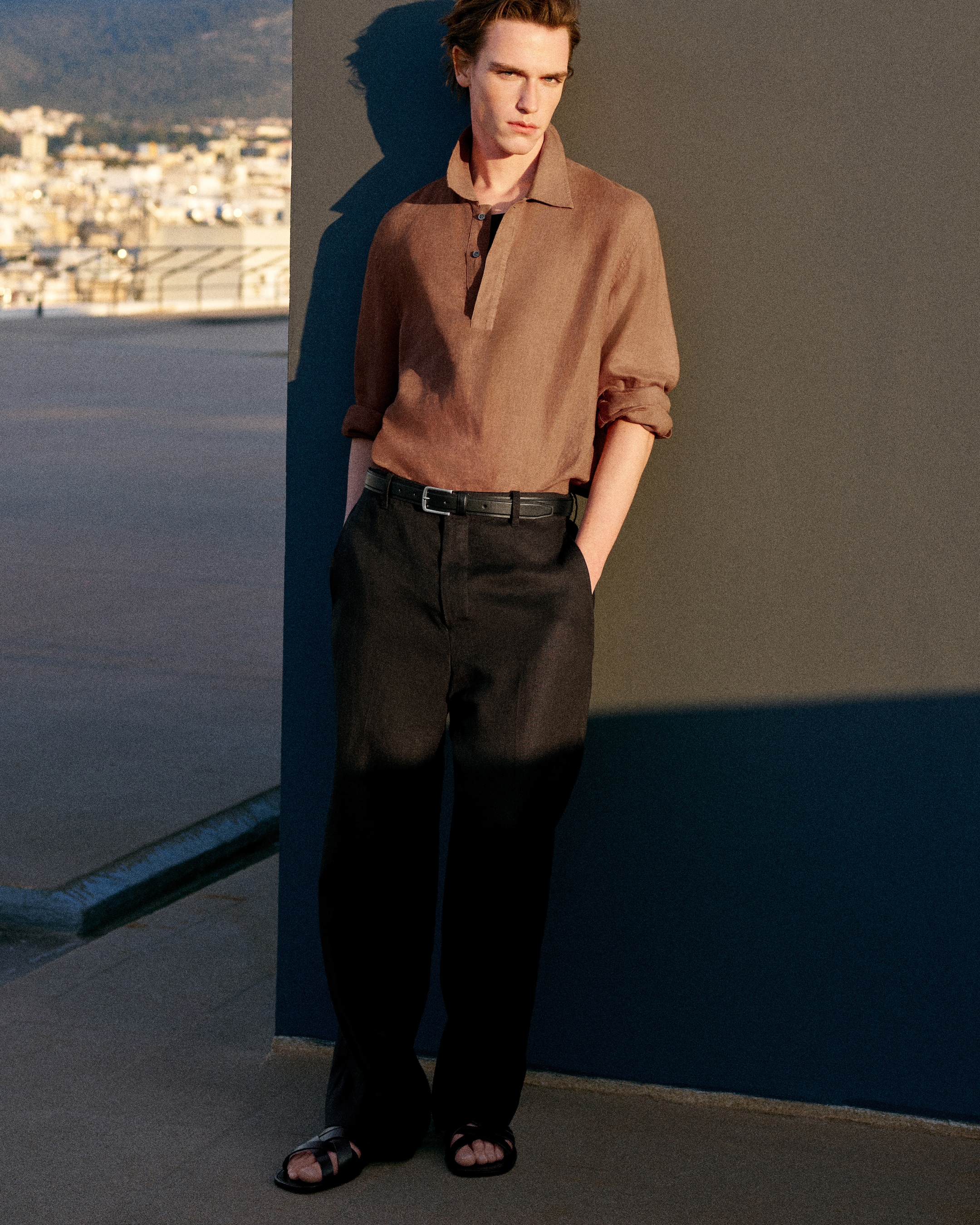brown linen pull over polo with long sleeves wearing brown trousers and sandals