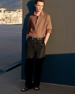 Placeholder for: brown linen pull over polo with long sleeves wearing brown trousers and sandals
