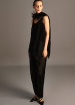 Placeholder for: A woman in an all-black outfit with a feathered shawl and pointed shoes, standing against a plain background.