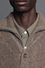 Placeholder for: Close-up of a person wearing a brown wool jacket over a beige buttoned shirt, with a focus on the textures and layers of clothing.