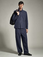 Placeholder for: A person wearing a blue matching jacket and trousers, holding a black backpack over one shoulder, standing against a plain background.