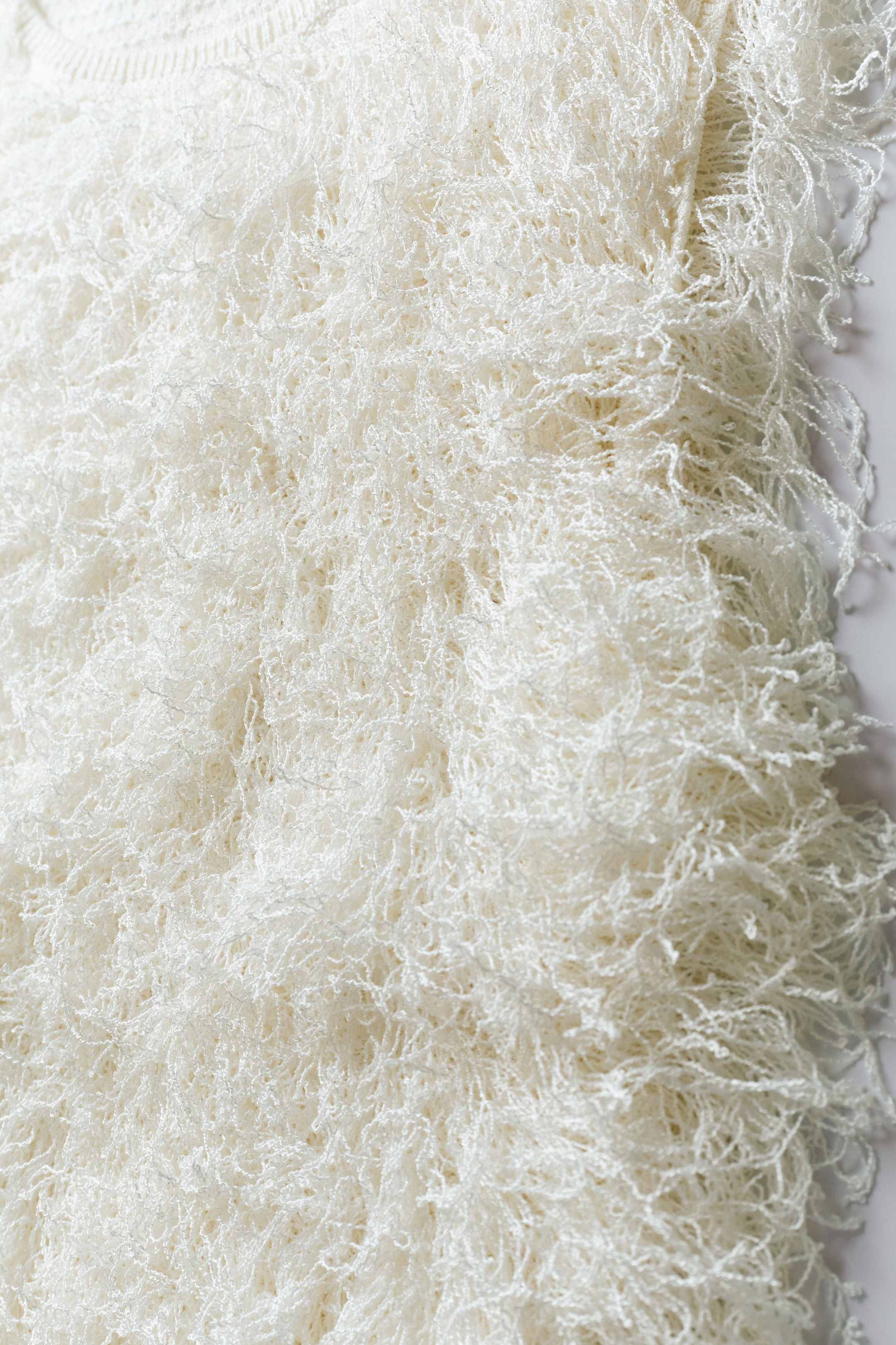 Close-up of a white, fluffy shaggy fabric texture with intricate, looped fibers creating a soft and textured appearance.