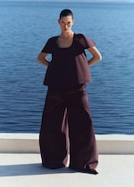 Placeholder for: Person in a burgundy outfit stands confidently by the sea, with a clear blue sky and water as the backdrop.