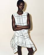 Placeholder for: A person wearing a sleeveless plaid dress with arms crossed, standing against a neutral background.