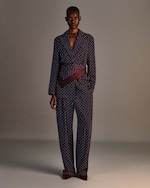 Placeholder for: Person in a polka dot suit with a purple sash stands against a neutral background, projecting elegance and style.