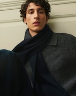 Placeholder for: A person with curly hair wearing a dark scarf and a wool sweater, seated against a neutral background.