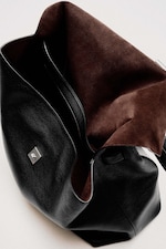 Placeholder for: Black leather handbag with an open top revealing a brown suede interior, featuring a small silver square clasp on the exterior.