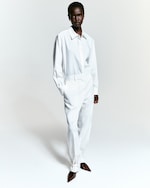Placeholder for: Person in a stylish white outfit with a collared shirt and high-waisted pants, paired with pointed brown shoes, standing confidently.