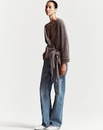 Placeholder for: A person wearing a gray fuzzy cardigan with a belt, blue wide-leg jeans, and white shoes, posing against a plain white background.