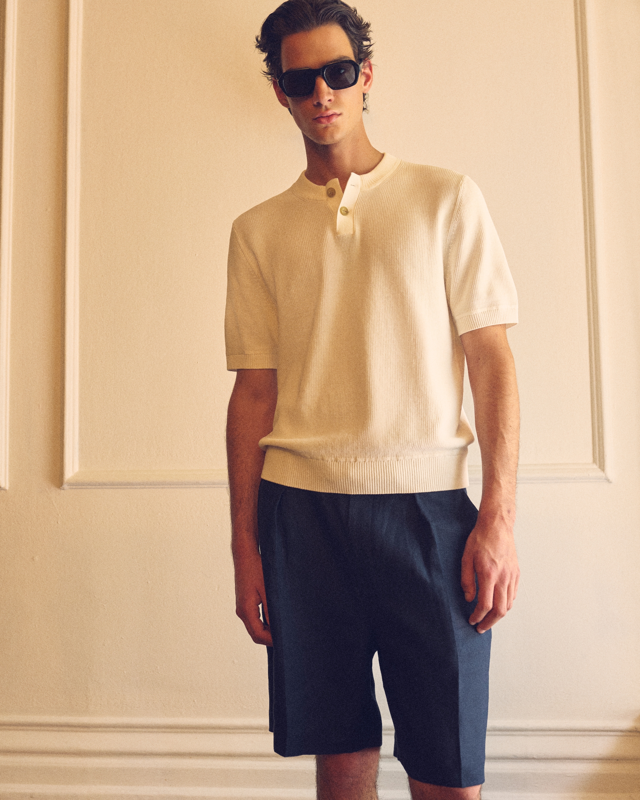 Man standing with a collared knitted top on, navy trousers & sunglasses