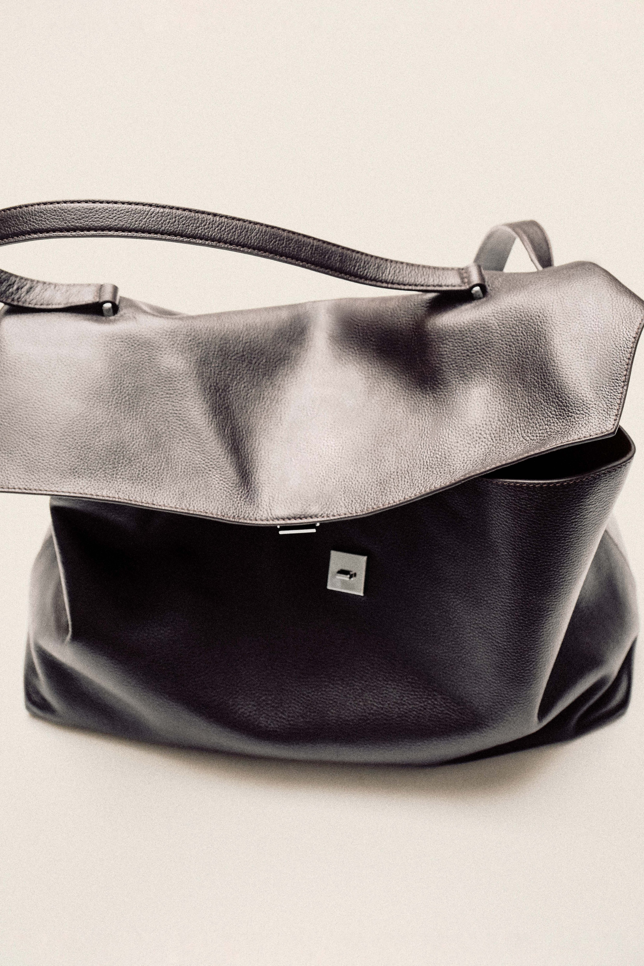 Sleek black leather handbag with an adjustable strap and a simple clasp, resting against a neutral background.