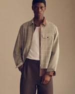 Placeholder for: A man wearing a plaid jacket over a white shirt and brown pants, standing against a plain background.