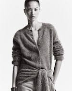 Placeholder for: A monochrome image of a person wearing a fuzzy buttoned cardigan and jeans, with hair tied back, gazing directly at the camera.