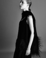 Placeholder for: A monochrome side profile of a person wearing a black outfit with feathered details, their hair pulled back, against a gray background.