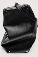 Placeholder for: Black textured leather handbag with a single strap, square metal accents on the base, placed on a light background.