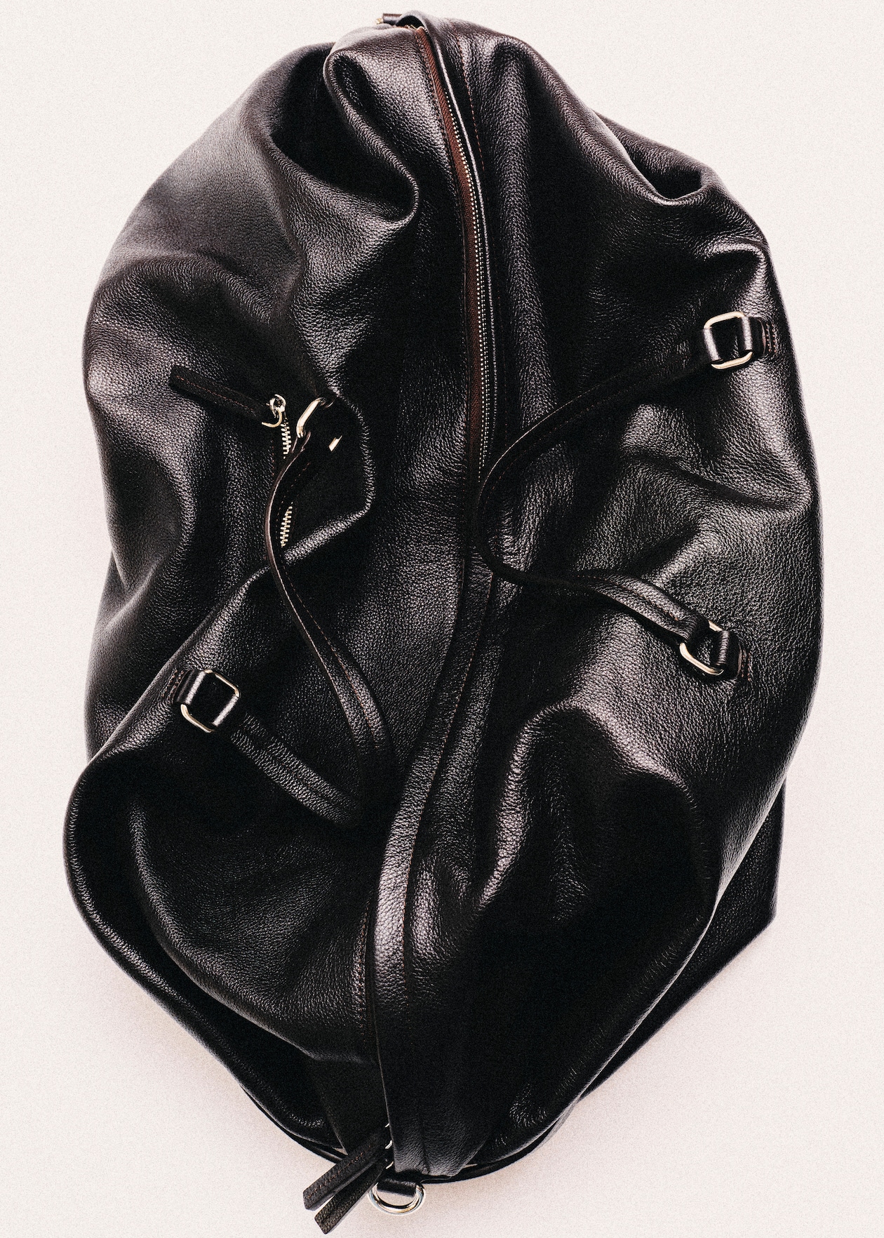 A crumpled black leather bag with prominent zippers and straps, showcasing a glossy texture against a light background.