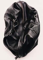 Placeholder for: A crumpled black leather bag with prominent zippers and straps, showcasing a glossy texture against a light background.
