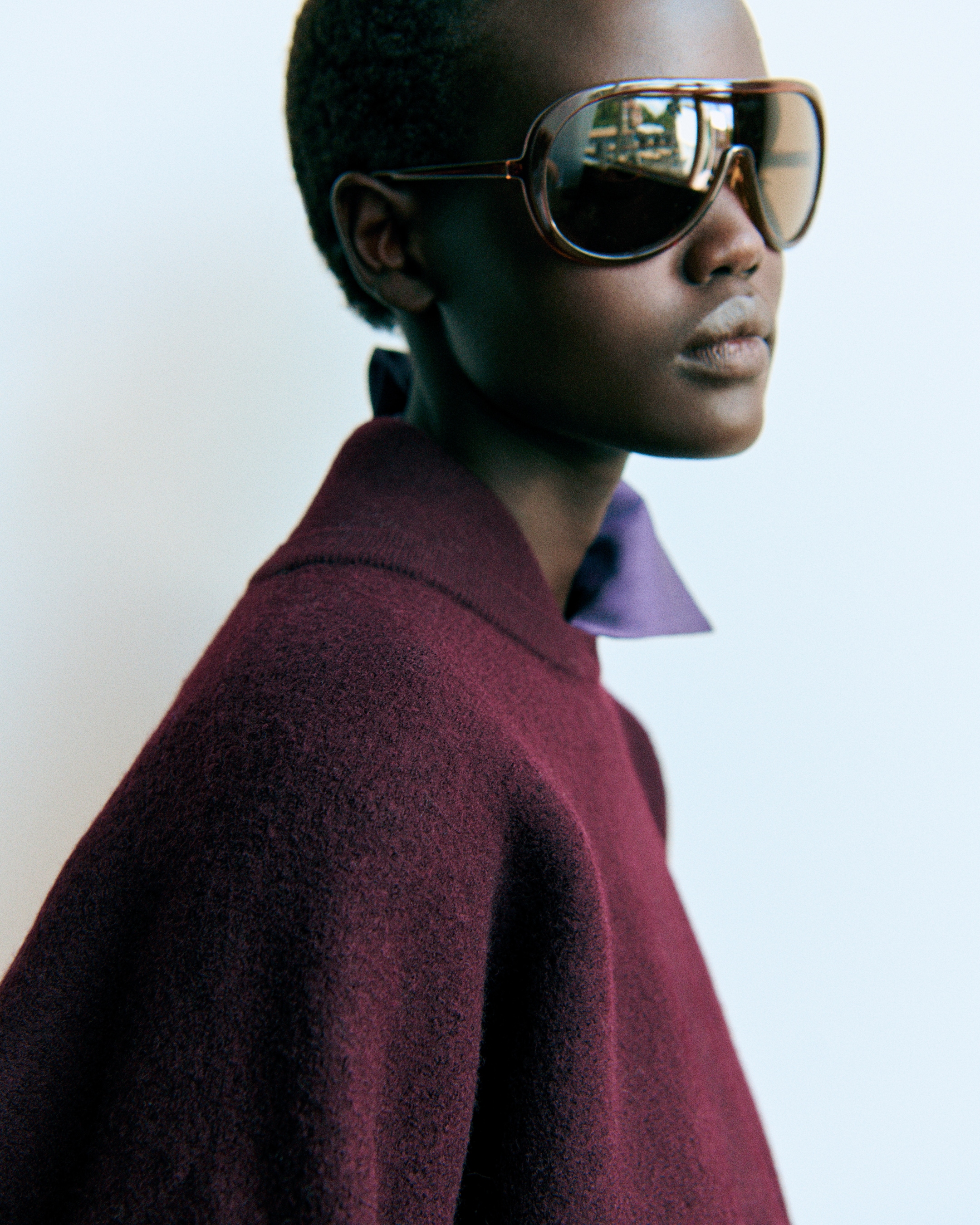 A person wearing large, dark sunglasses and a maroon sweater posed against a light background.