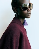 Placeholder for: A person wearing large, dark sunglasses and a maroon sweater posed against a light background.
