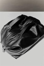 Placeholder for: Black leather duffel bag with two handles and a zipper, placed on a light surface, casting a subtle shadow.