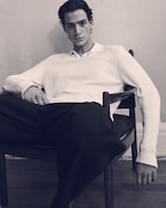 Placeholder for: Black & white image of a man in a knitted white polo shirt & black trousers on, sitting down