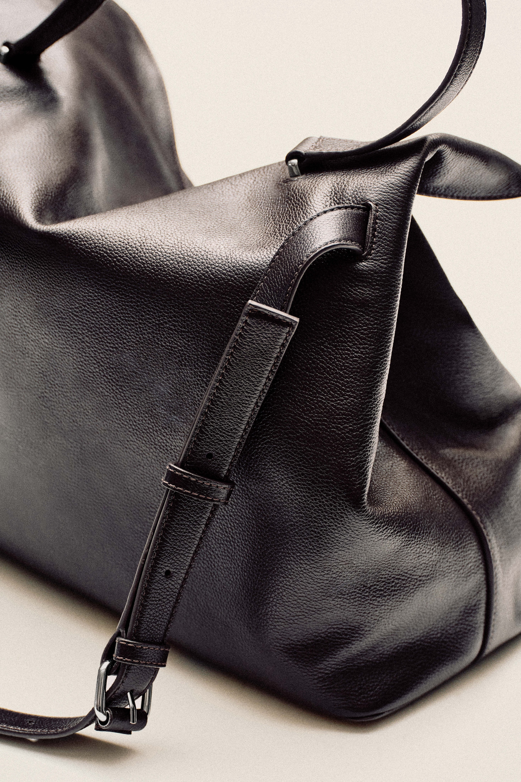 A close-up of a black leather bag with a glossy finish, featuring adjustable straps and silver buckle details.