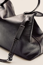 Placeholder for: A close-up of a black leather bag with a glossy finish, featuring adjustable straps and silver buckle details.