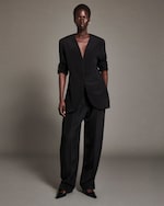 Placeholder for: A person wearing an elegant black suit with a deep V-neck, buttoned front, and pants, standing confidently against a neutral background.