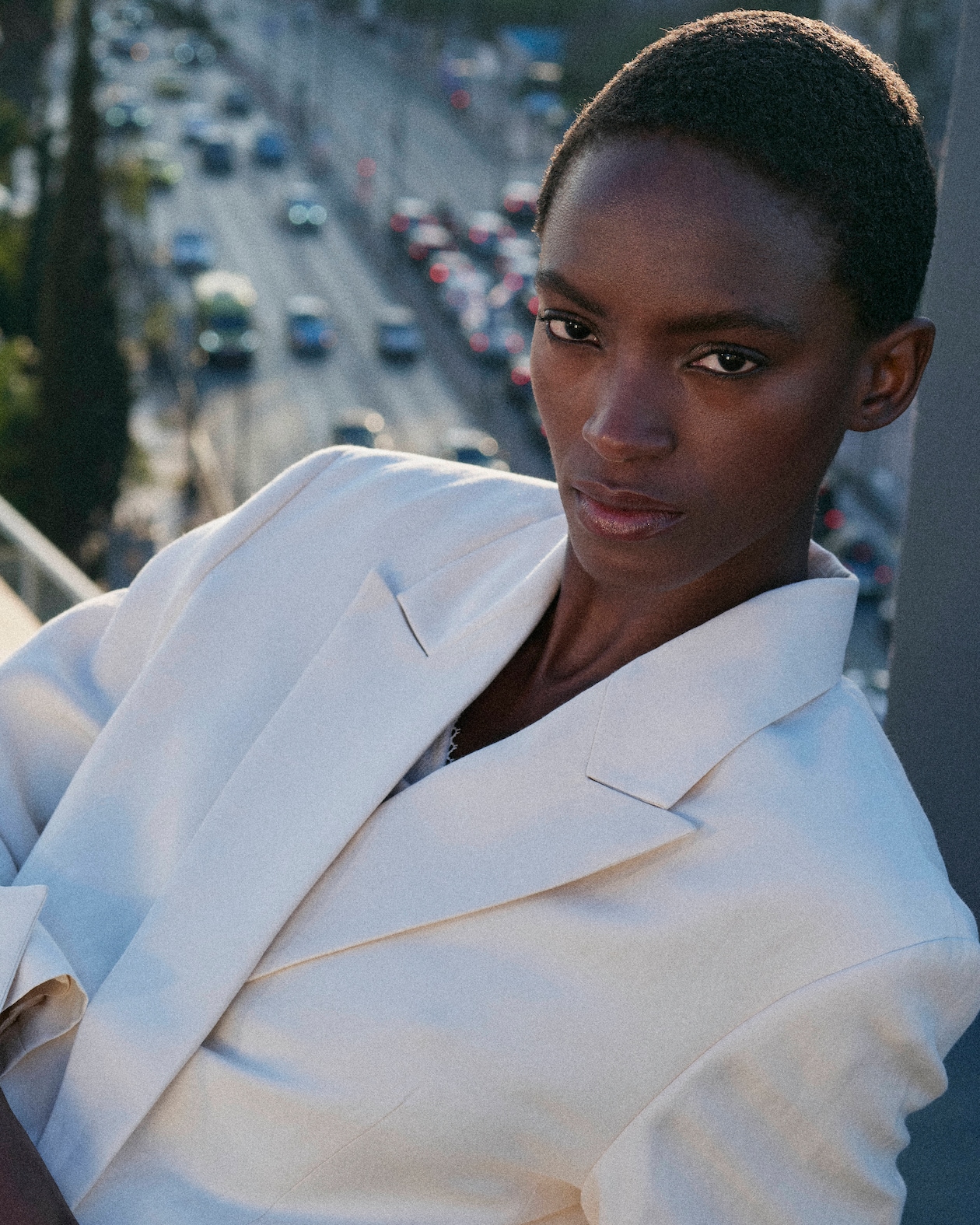 Person in a white linen blazer poses confidently, with a city street and cars in the blurred background.