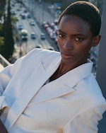 Placeholder for: Person in a white linen blazer poses confidently, with a city street and cars in the blurred background.