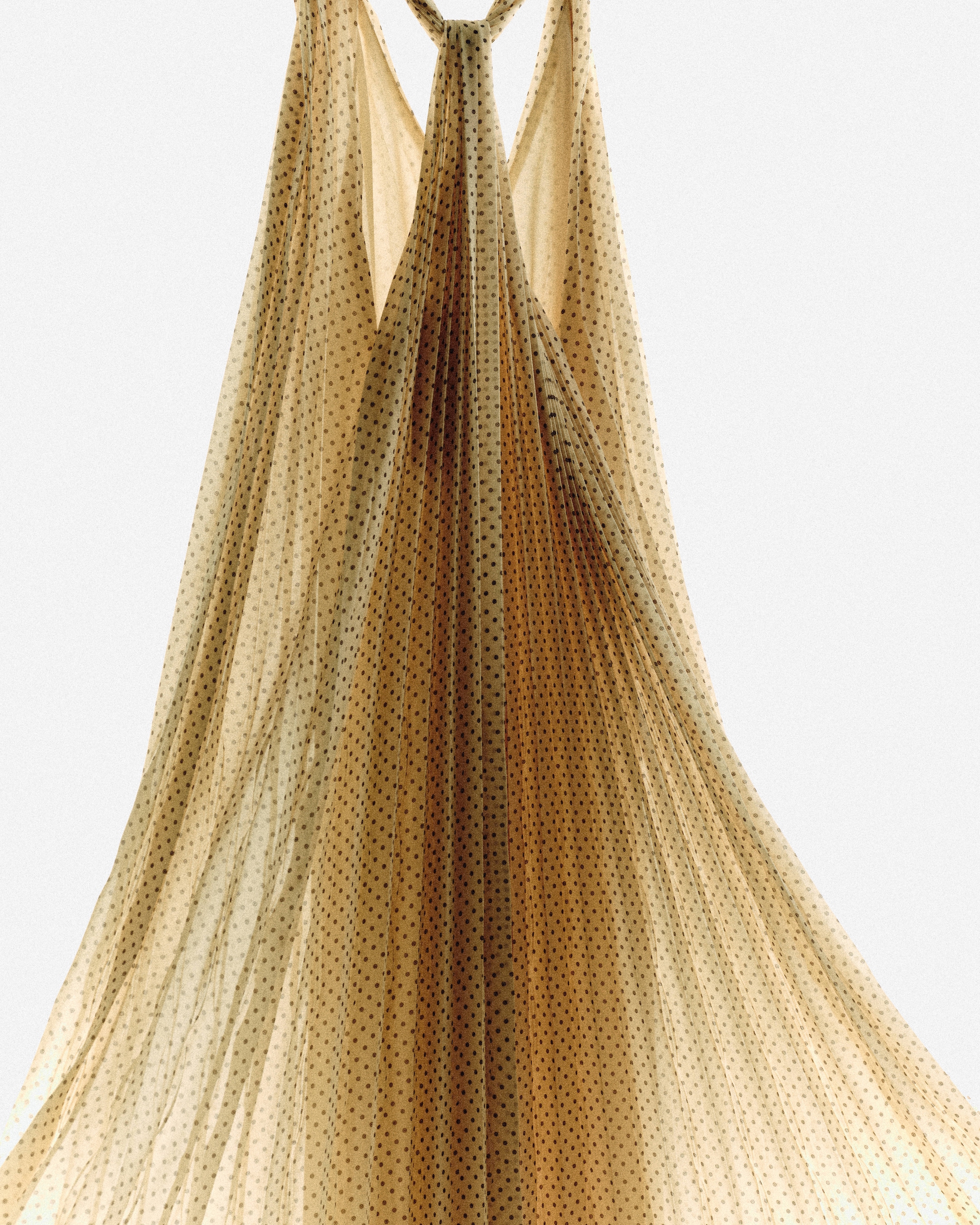 A flowing beige polka dot dress hangs gracefully, showcasing its sheer, draped fabric against a neutral background.