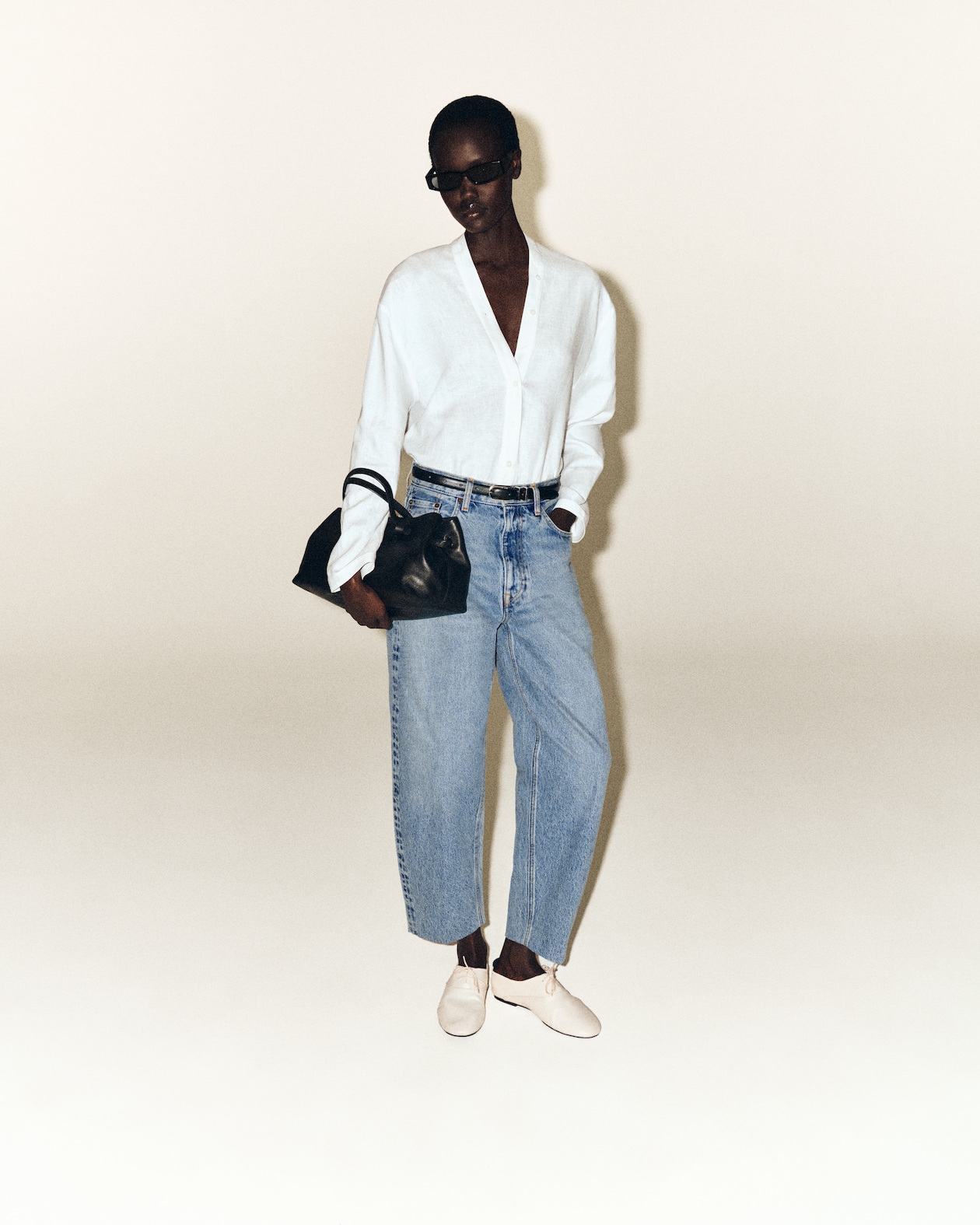 woman in white v-neck shirt with blue jeans holding a black bag with white shoes