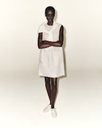 Placeholder for: woman in beige sleeveless dress with jumper on shoulders, sunglasses and white shoes