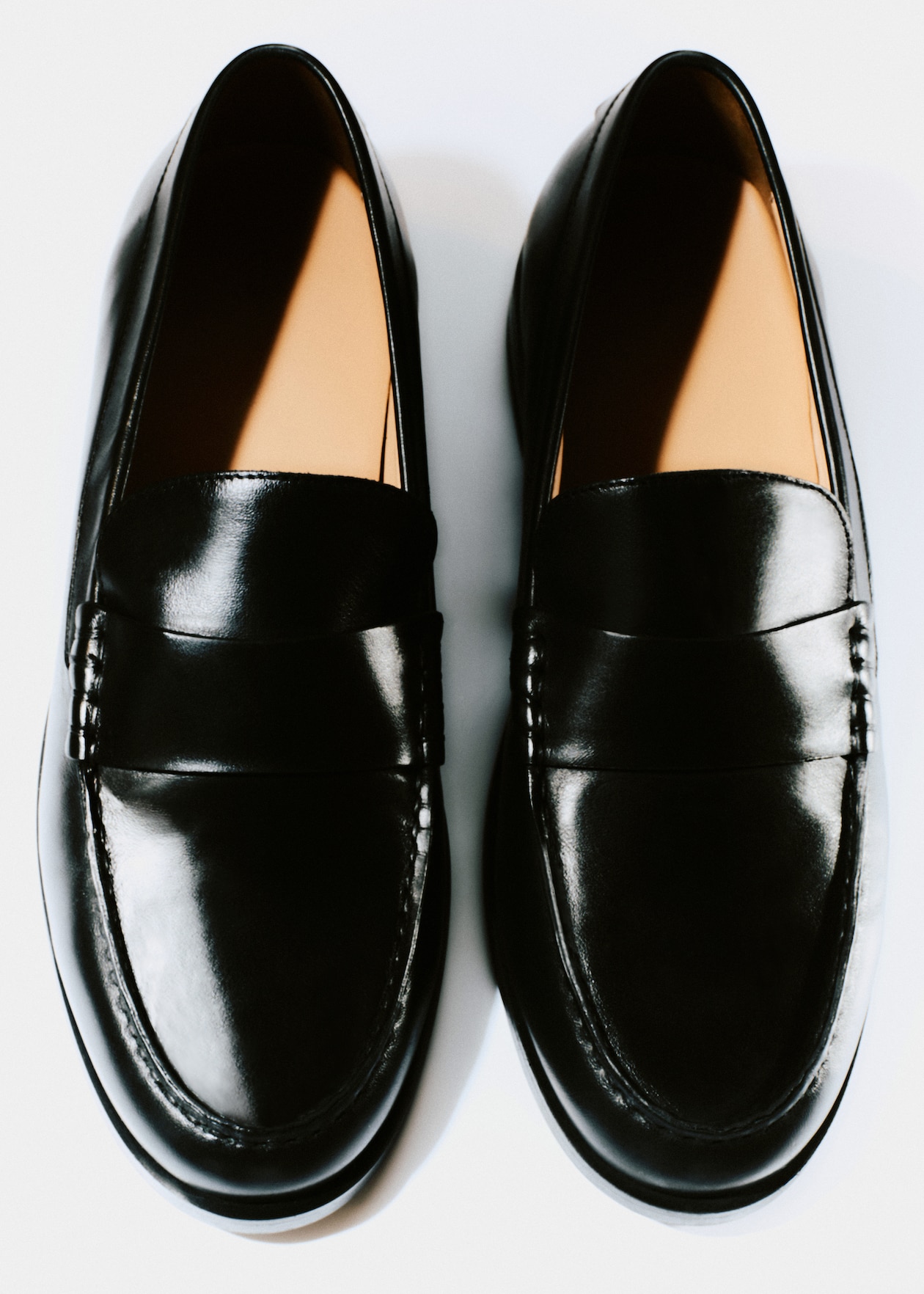 A pair of shiny black leather loafers with tan-colored interiors, viewed from above on a white background.