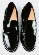 Placeholder for: A pair of shiny black leather loafers with tan-colored interiors, viewed from above on a white background.