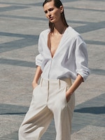 Placeholder for: A person in a white shirt and beige pants stands confidently, hands in pockets, against a tiled outdoor backdrop.