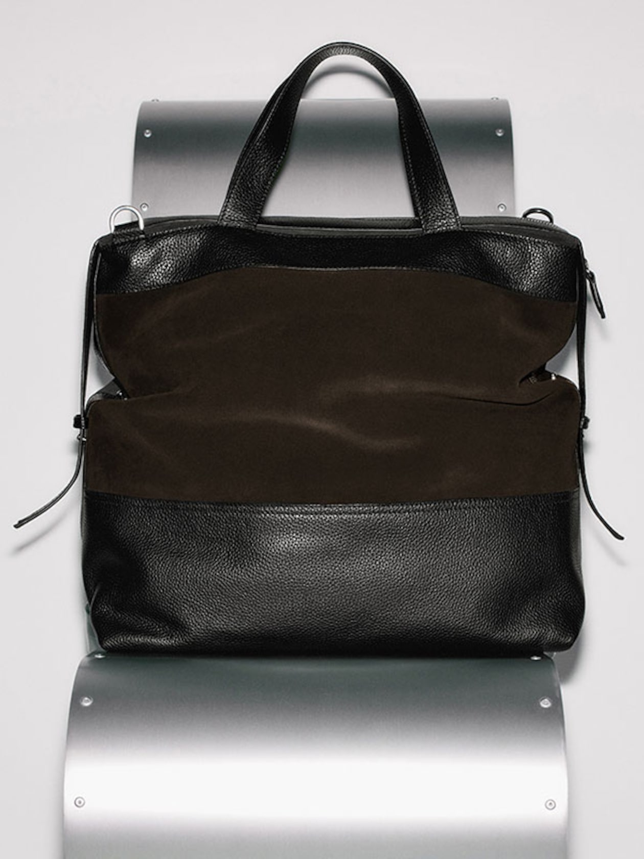 A sleek black and brown leather tote bag with double handles, displayed against a metallic background.