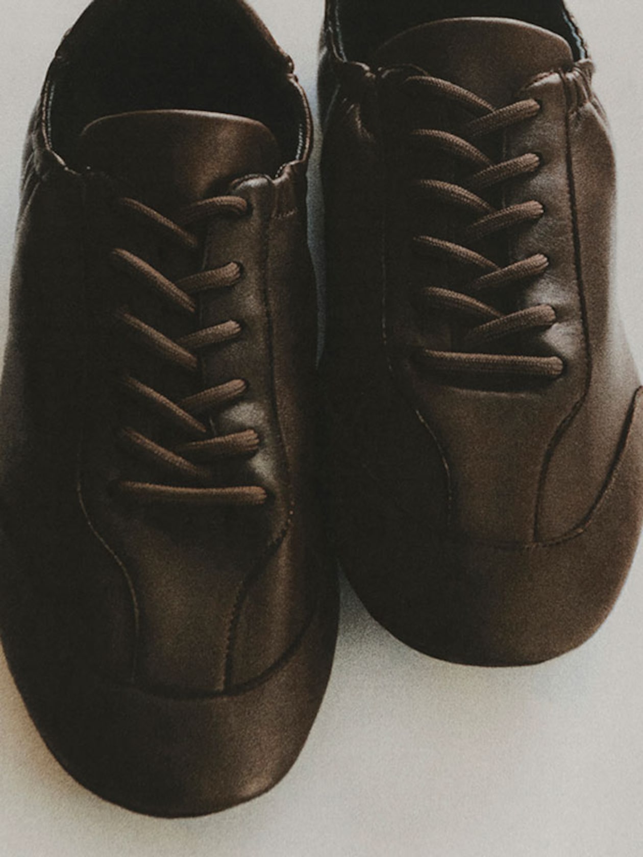 A pair of brown leather sneakers with black laces, viewed from above, placed on a light surface.
