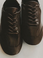 Placeholder for: A pair of brown leather sneakers with black laces, viewed from above, placed on a light surface.