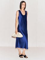 Placeholder for: Woman in a sleeveless, blue satin dress holds a white clutch and wears black heeled sandals against a simple background.