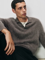 Placeholder for: Person in a cozy gray sweater and dark pants sits pensively against a white background.