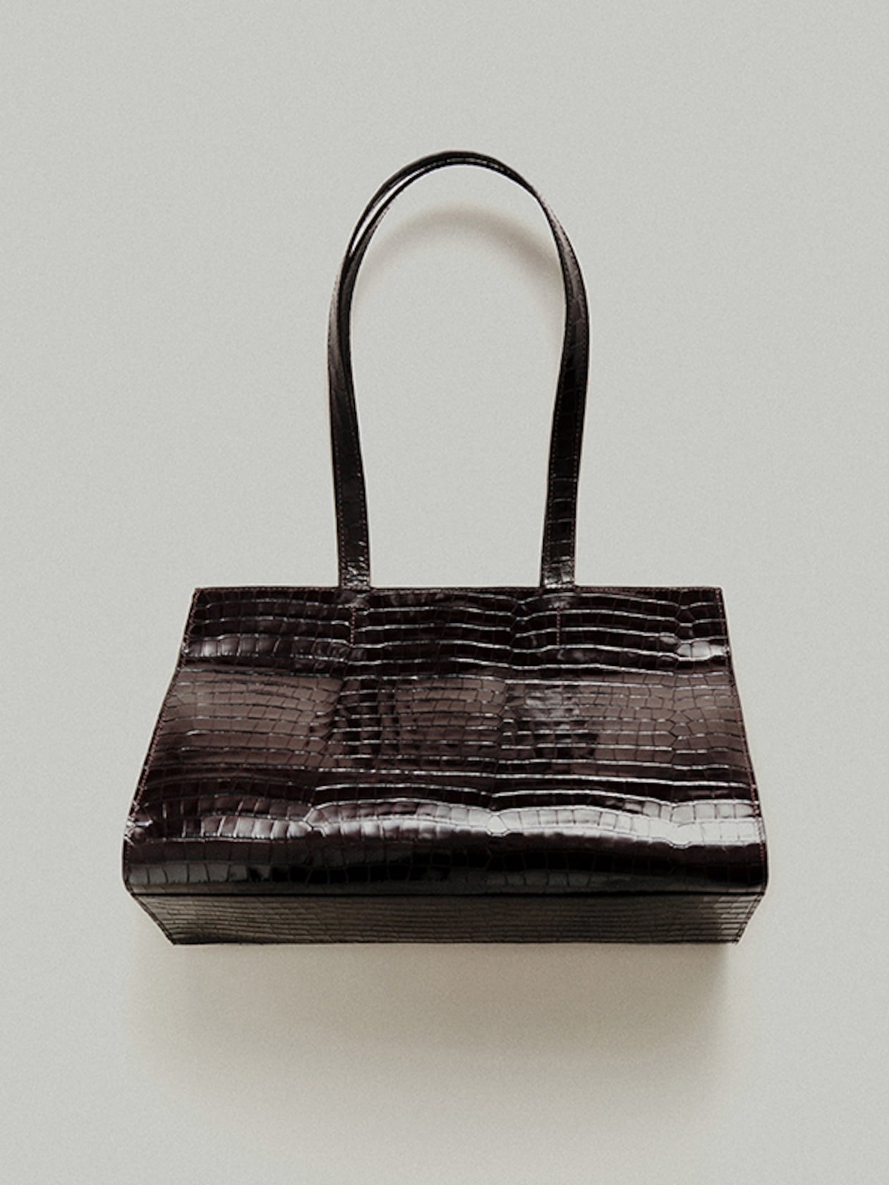 Dark brown crocodile-patterned handbag with long, slim handles against a plain background.